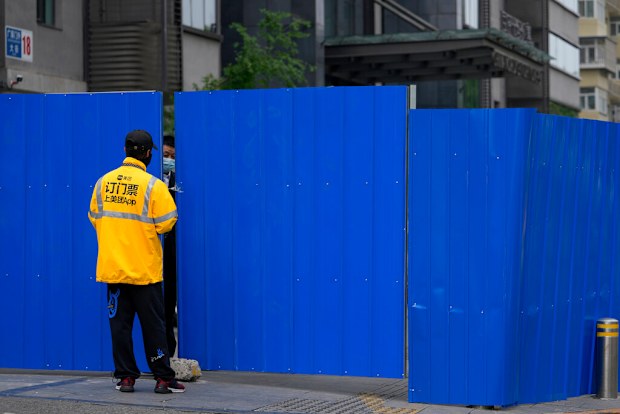 A delivery worker chats with a masked security guard at a barricaded fence of a locked-down residential complex.