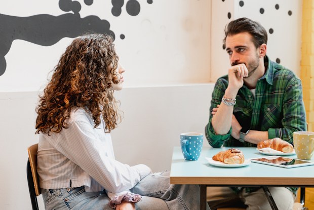 Young couple sitting at table in a cafe talking with serious faces.