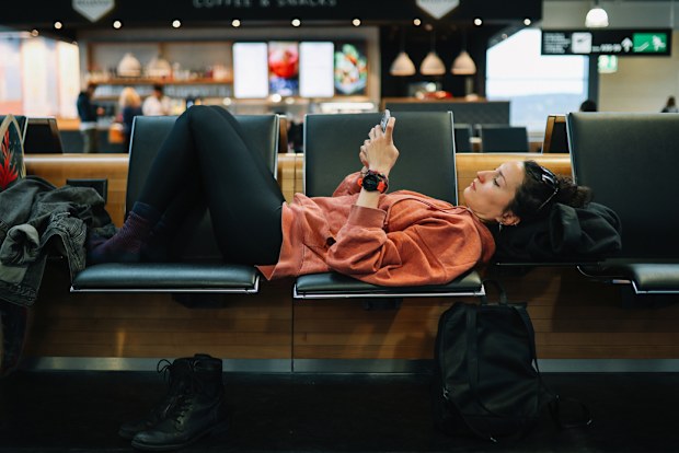 Woman relaxing at the airport, reading stuff on her smartphone, having a long layover.