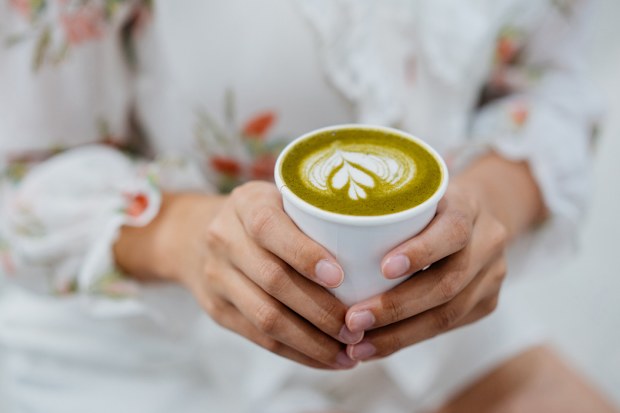 An Asian Chinese woman holding a cup of matcha latte in a cafe and ready to drink.