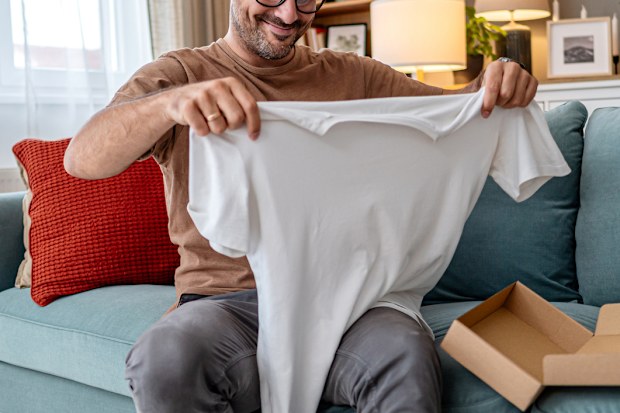 Cheerful young man unboxing clothes after online shopping
