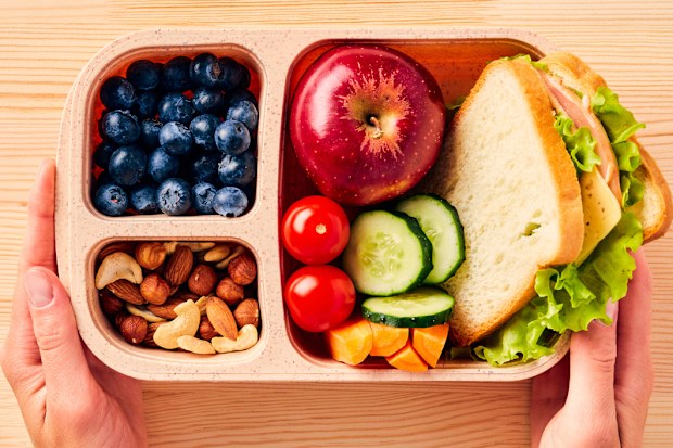Women's hands hold lunchbox of healthy food over wooden table.