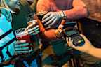 Diverse friends in bar paying with cellular device