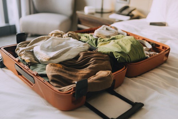 An open, packet suitcase on a bed with white sheets.