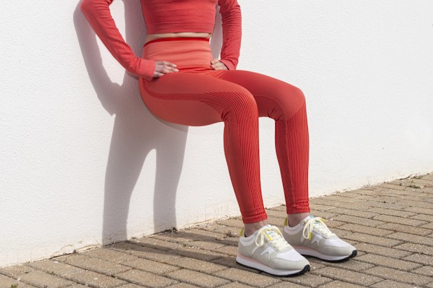 Sporty woman doing squats against a white wall outside in the sun.