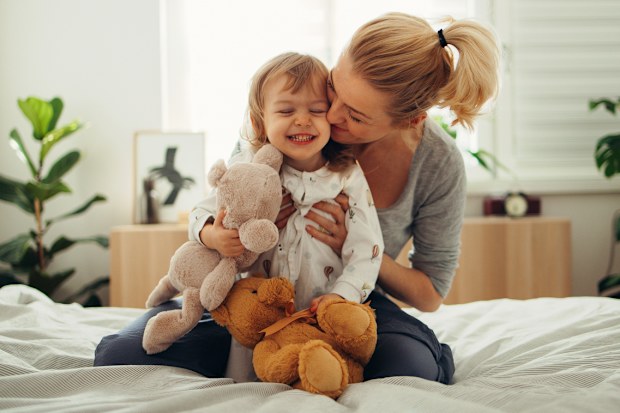 Mum holding toddler playing on a bed