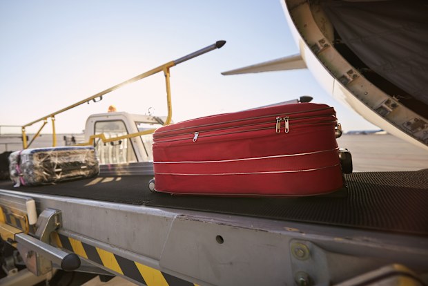 Loading of luggage to airplane. Red suitcase on conveyor belt at airport.