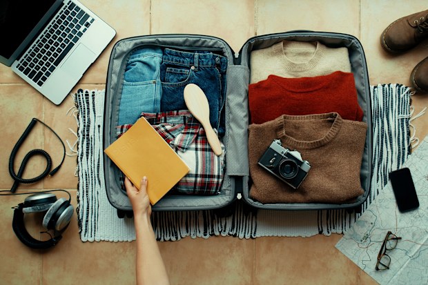 Woman packs winter themed suitcase for autumn holiday. Vacation preparation, careful bag packing. Millennial generation z travel blogger pack suitcase with social media vintage camera, sweater, laptop