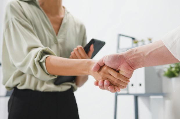Multiracial group of young creative people in smart casual wear discussing business shaking hands together and smiling while standing in modern office. Partner cooperation, coworker teamwork concept.