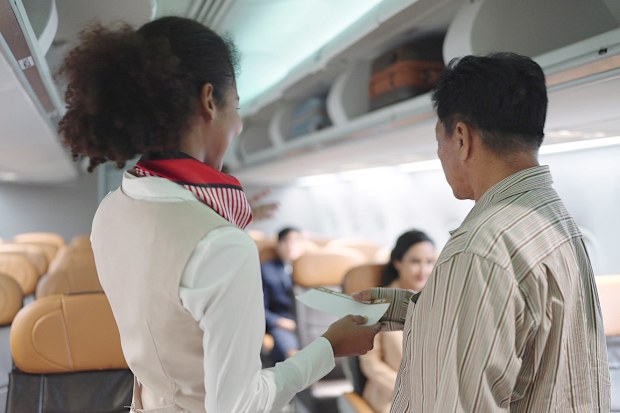 Back view of women flight attendant checking passenger's boarding pass and welcoming to the flight. Woman cabin crew greeting passengers on airplane service. Airways concept