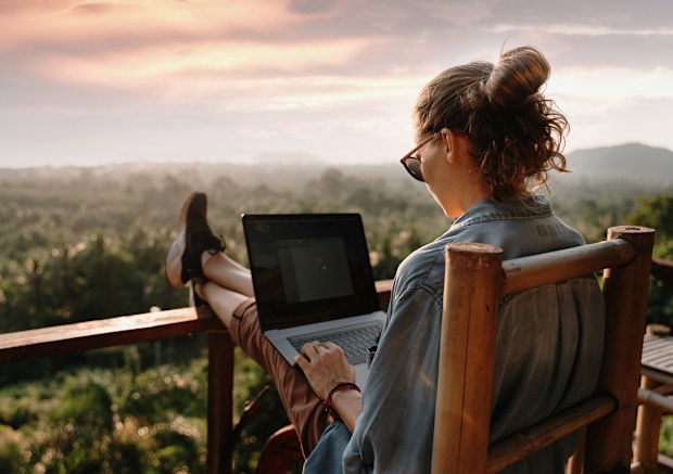 Young business woman working at the computer in cafe on the rock. Young girl downshifter working at a laptop at sunset or sunrise on the top of the mountain to the sea, working day.