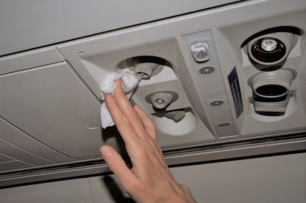 Photo showing woman's hand cleaning the air vents in an airplane with a white disinfectant wipe