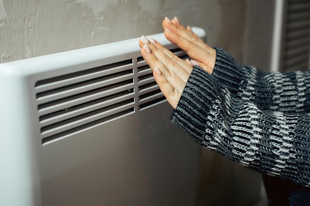 Woman holding hands to heater winter bills energy prices living in poverty cold weather