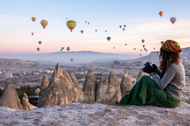 Young women (solo traveller) shooting photos of hot air balloons flying in red and rose valley in Goreme in Cappadocia in Turkey stock photo