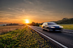 Motion blurred car driving on the asphalt road in rural landscape at sunset