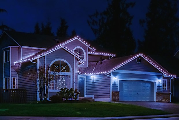 Night time photo of a modern American suburban home decorated with festive Christmas holiday lights and red ribbons on garage doors