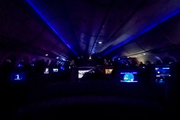 Medium shot night scene inside an airplane showing rows of seats with backrest screens.