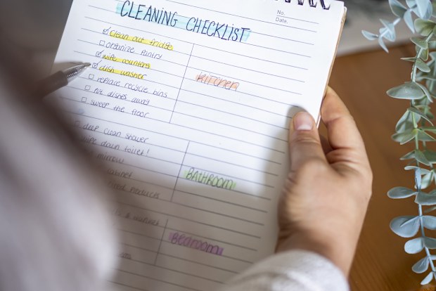 Woman planning a spring cleaning checklist routine for household. Handwriting To-do list for organize housecleaning with check marks for motivation. Tidy and domestic life.
