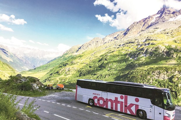 A Contiki-branded bus driving along a mountainous road.