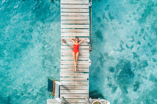 Woman in swimsuit sunbakes on boardwalk over turquoise water
