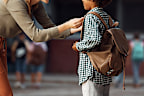 Happy mother greeting with her African American son on first day of school in the schoolyard.