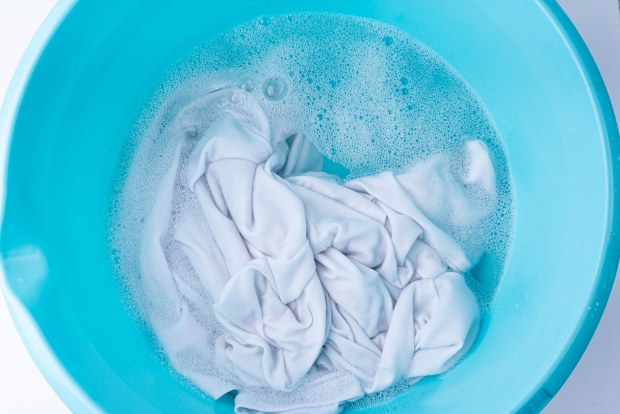 Hand laundry washing clothes in blue plastic basin, soaked white cloth handwash, housework