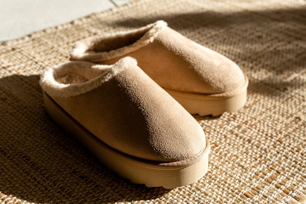 One pair of modern fashionable warm Uggs slippers on a high platform lie in the center on a woven jute rug on a tiled floor on a winter day with shadows from the sun, close-up side view. Fashionable shoes concept.