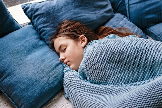 Young teenager girl sleeping snuggled in warm knitted blue blanket. Seasonal melancholy, apathy and winter blues. Cozy home.