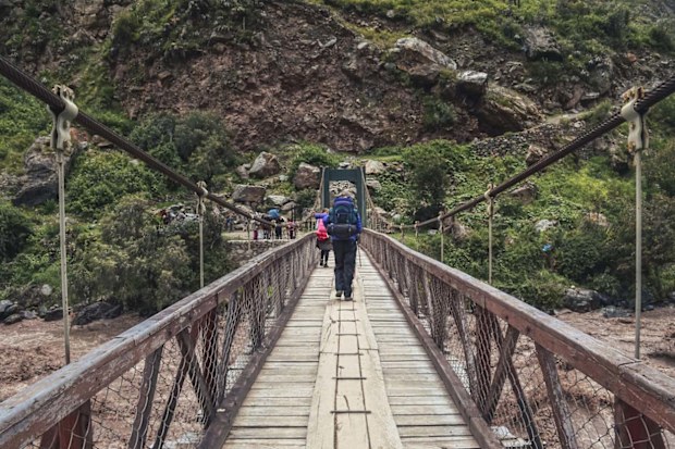 Male backpacker crossing the bridge over Vilcanota river to start inca trail to Machu Picchu archaeological site from the Inca's ancient civilization in Peru. South America