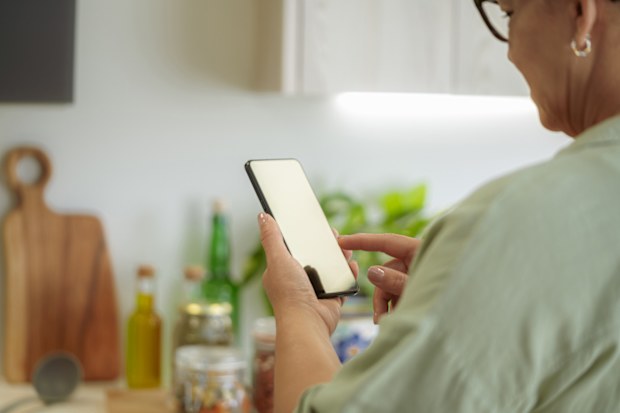 Close up of woman holding mobile phone in kitchen. Using phone.Text messaging. Reading message