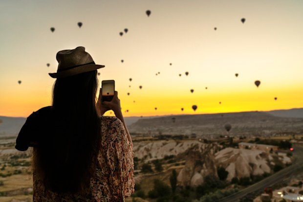 Woman using iPhone to photograph landscape on holiday