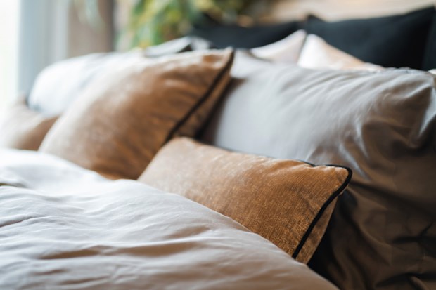 Bed maid-up with clean white pillows and bed sheets in beauty room. Close-up. Lens flair in sunlight.Closeup of new bed comforter with decorative pillows, headboard in bedroom in staging model home