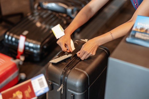 Check-in employee attaches a luggage tag to suitcase of passenger. Close up of hands.