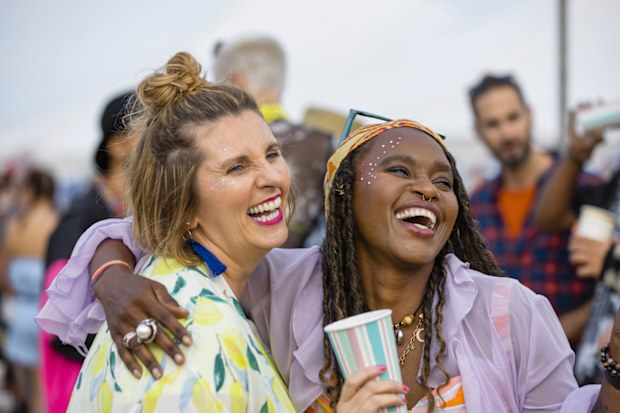  Group of mixed age and ethnic friends having fun at a festival in Northumberland, North East England. They are laughing and drinking together with their arms around each other.