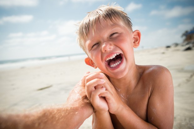 Blonde boy tickled and laughing at the beach, happy as can be.