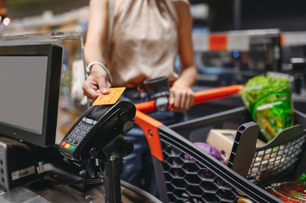 Cropped close up woman hand shopping at supermaket put credit card to wireless modern bank payment terminal process acquire payments near cashier checkout with cart inside store. Purchasing concept
