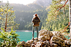Enjoying a peaceful moment, a woman sits on a rocky ledge while gazing at the stunning turquoise lake surrounded by lush mountains during daylight. Active lifestyle.