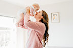 Proud young mother holding up baby close to face and smiling in living room