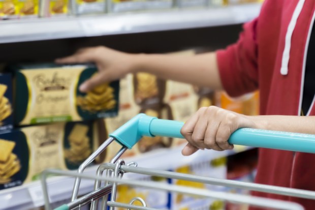 Woman using trolley cart while walking and taking products from shelf in a grocery store.