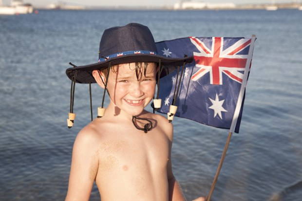 A cute young boy wearing an Australian cork hat and waving an Australian flag at the beach for Australia Day.
