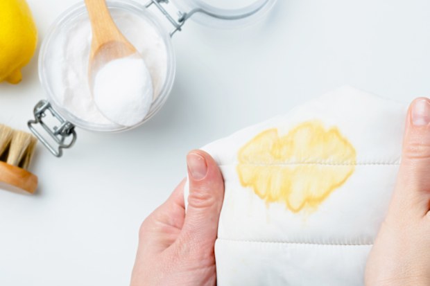 A person holding a stained piece of fabric near a bowl of baking soda and a lemon, showcasing a diy cleaning method using natural products to remove stains