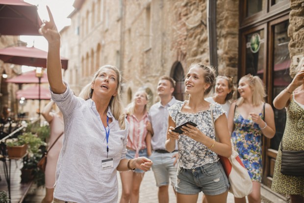 Medium group of people standing in a street in Volterra. They're listening to a tour guide who is talking about the architecture and the history.