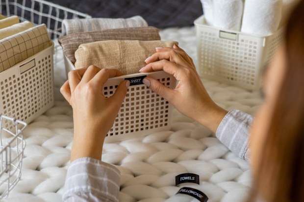 Woman hands neatly folded linens and towels use Marie Kondo method with sticky label tags top view closeup. Female housewife arms sticking names on case box for comfortable storage in bedroom closet