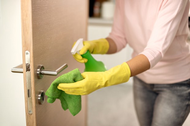 Woman cleaning door handle with disinfectant.