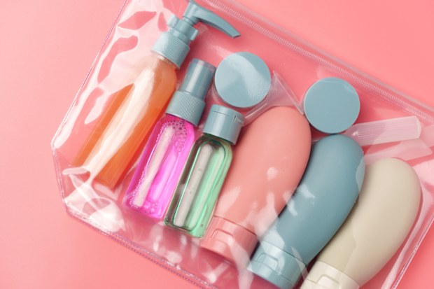 Clear Plastic Bag Containing Travel-Sized Toiletries on Pink Background close up