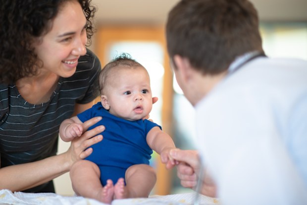 A mother holds her son in her arms while a male doctor gives him a checkup.