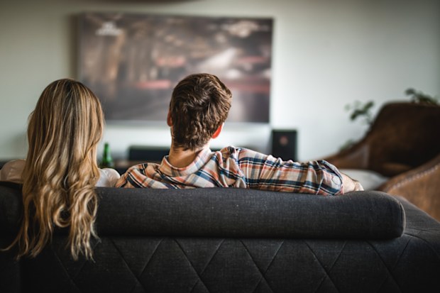 Rear view of a couple relaxing on sofa in the living room and watching a movie on TV