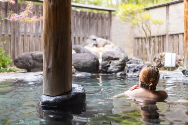 A rear view of a woman relaxing in a Japanese hot spring outdoor bath.