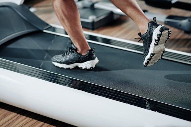 Close-up image of fit man in sneakers running fast on treadmill in gym in the morning
