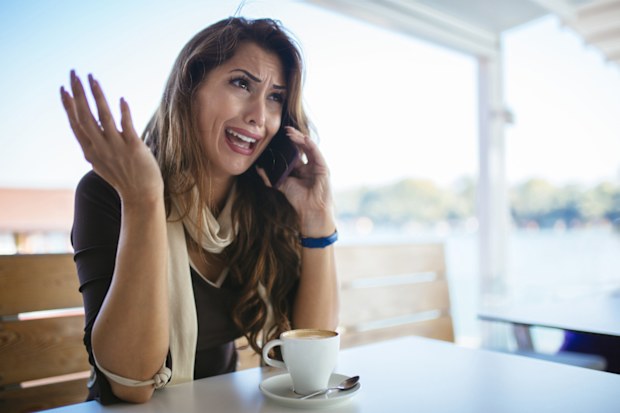 Young stressed woman freelancer talking on mobile phone at cafeteria